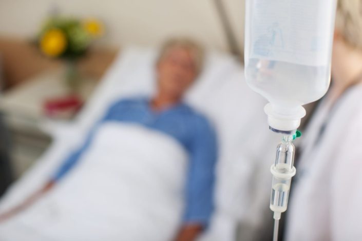 Close-up of an intravenous-drip bottle with doctor and patient in the background