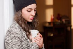 Sad-looking young woman with dysthymic disorder, or PDD, looks down while holding a mug.