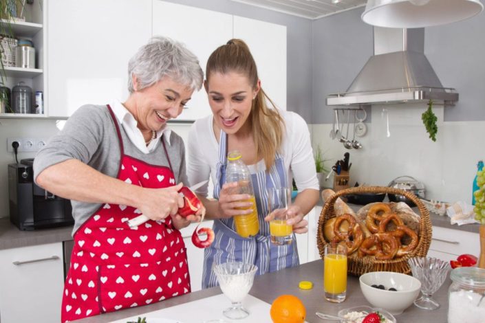 Senior mother and daughter making healthy breakfast together in kitchen.