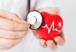 A doctor holding a stethoscope up to a toy heart