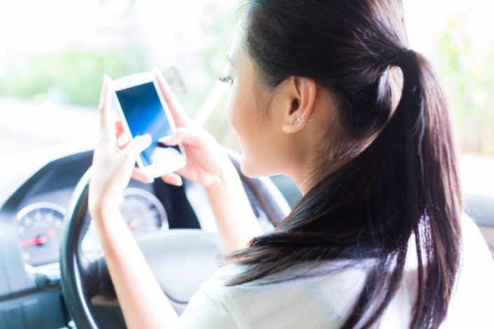 young woman texting message on mobile phone while driving car