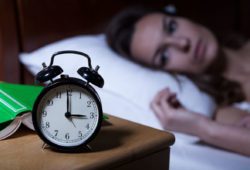 woman lying in bed stares at clock in the middle of the night