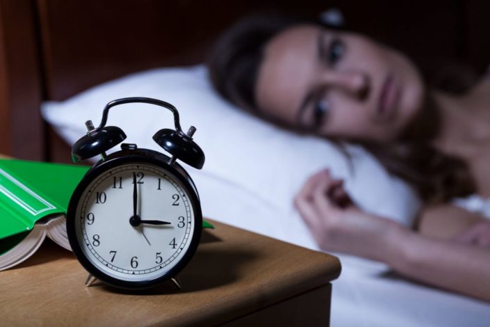 woman lying in bed stares at clock in the middle of the night