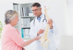 doctor and senior female patient look at a model of a spine