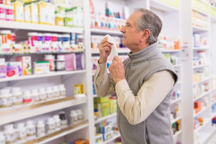 sick man holding tissue looks at OTC decongestants in a pharmacy
