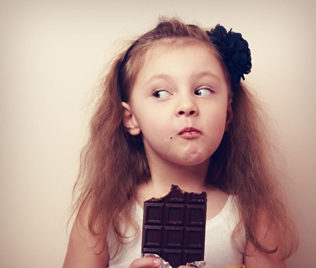 Girl eating large chocolate bar and looking to see if anyone is watching