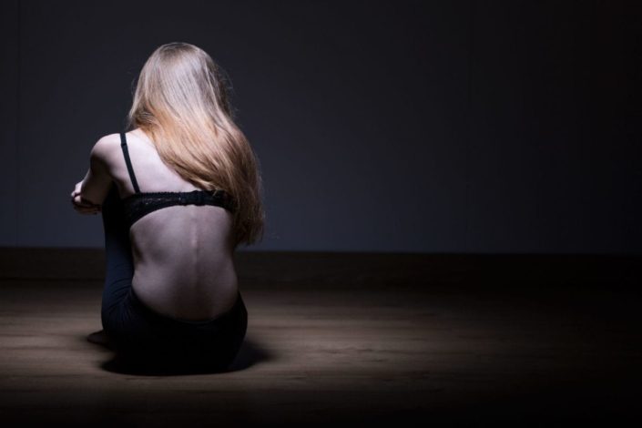 Woman sitting backwards on the ground showing her bony spinal column