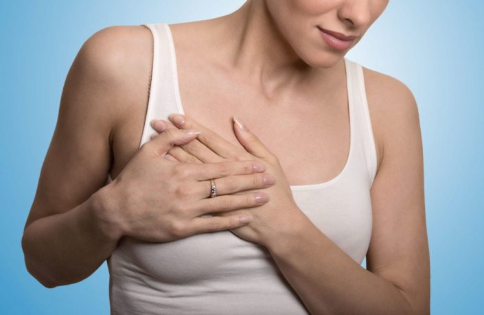 Close-up cropped portrait of young woman with breast pain touching chest