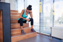 Tired woman sitting on the stairs with bottle of water in gym