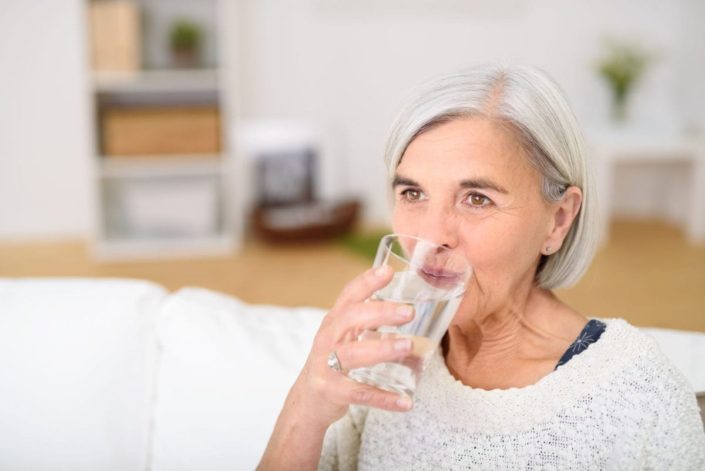 Middle-aged woman drinks a glass of water in the living room. Diabetes insipidus is a hormone disorder that causes extreme thirst and increased urination. It can be treated with medication.