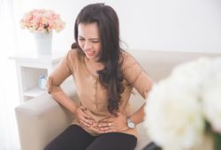 A woman frowning and grabbing her lower abdomen while sitting on the couch