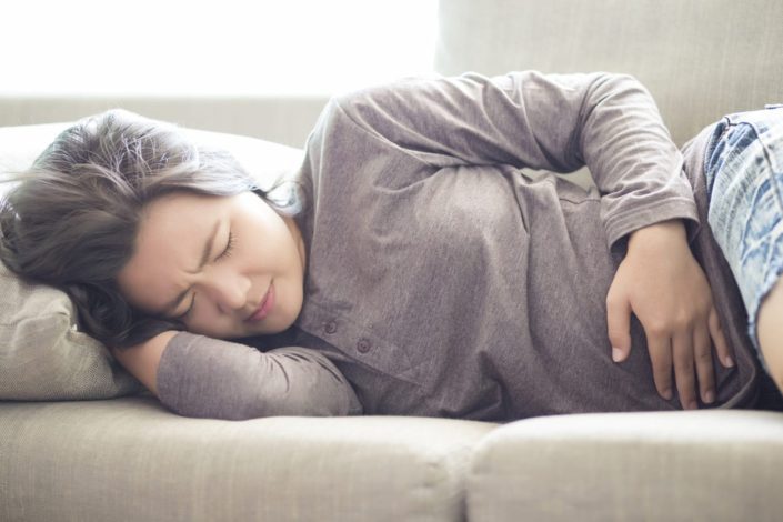 A woman who suffering from PMS is lying on the sofa with her hand on her abdomen.