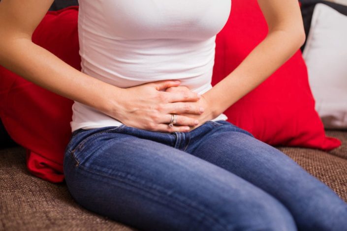 Woman suffering from menstrual cramps holds her stomach while sitting on couch. Dysmenorrhea is the medical term for pain that women have before or during menses (known as their period). It usually is not serious.