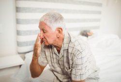 Older man, who can’t sleep at night, sitting on bed while spouse sleeps