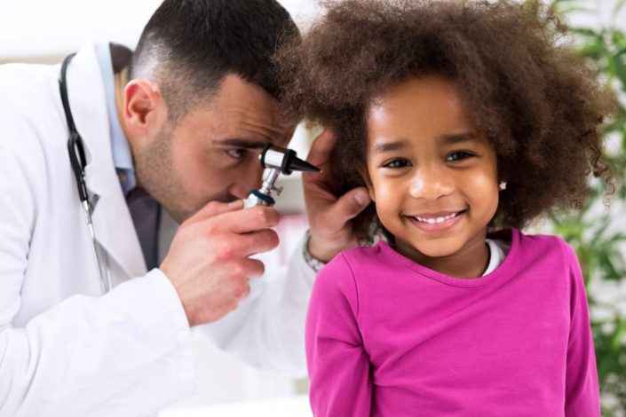 doctor examining the ear of a young smiling girl