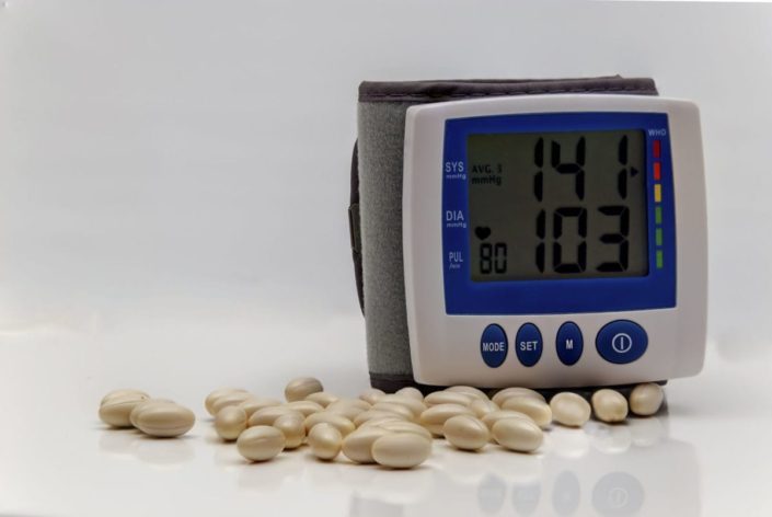 blood pressure monitor showing elevated readings with pills on a table