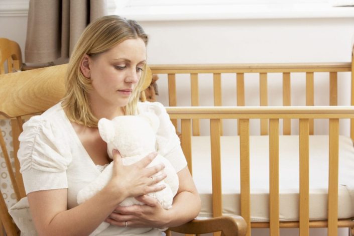 A sad woman holds a teddy bear in an empty nursery. An early pregnancy loss is a miscarriage that occurs on its own during the first 20 weeks of the pregnancy.