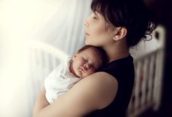 mother stands in nursery holding sleeping newborn
