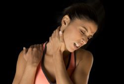 a young athletic woman grips her neck and shoulder and grimaces in pain