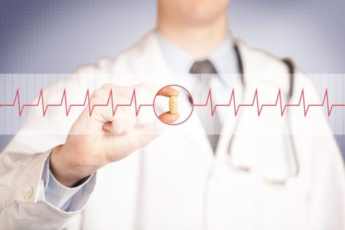 close-up of a doctor holding a pill, focused on a heartbeat graph