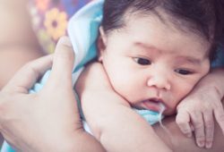 Mother burping her newborn baby girl, who has milk coming out her mouth.