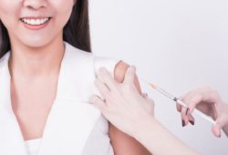 A woman with dark colored hair, wearing a white shirt receiving vaccination