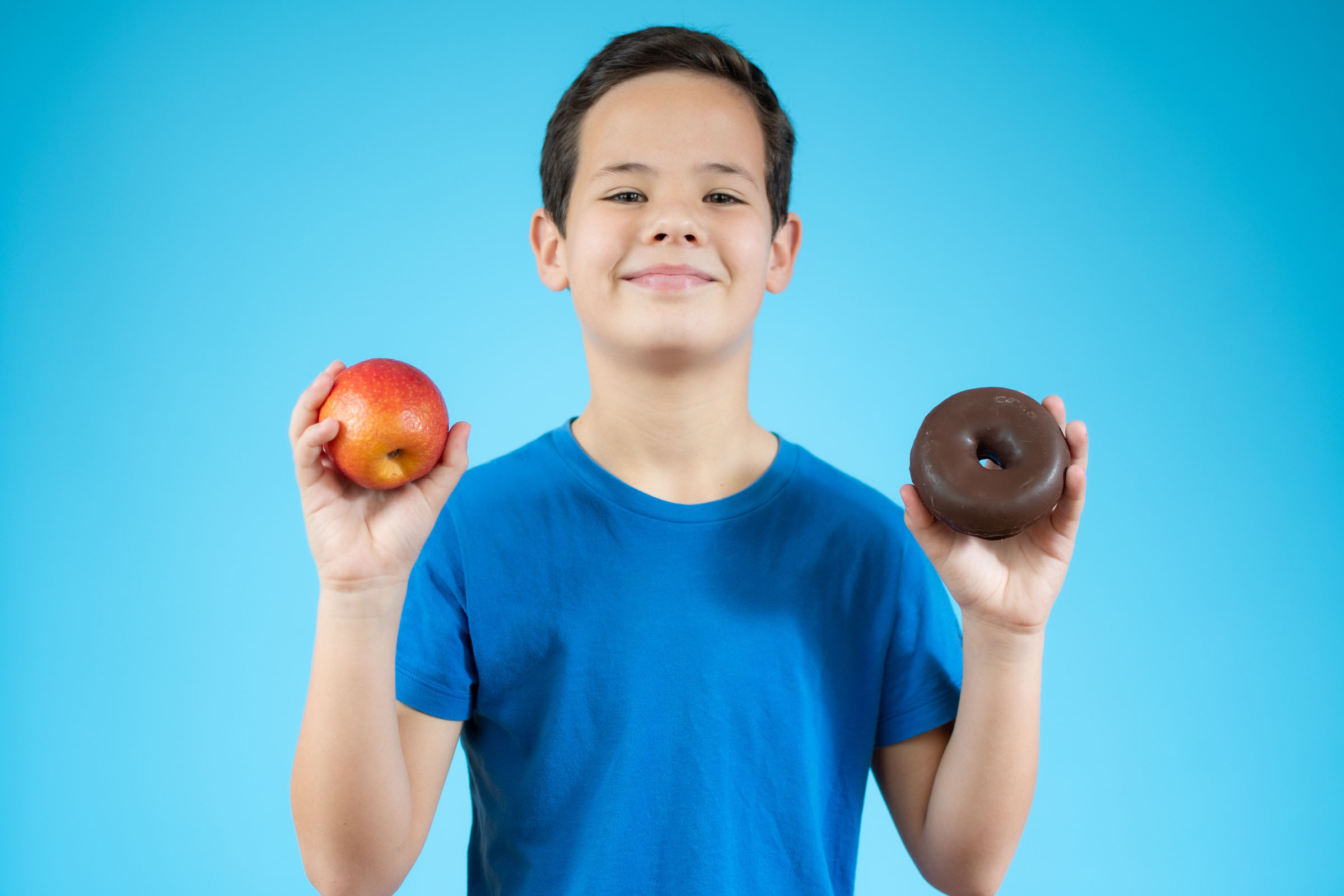 Young boy choosing between an apple and donuts