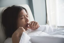 A woman is coughing on her bed. Finding the best cough suppressant can be a challenge.