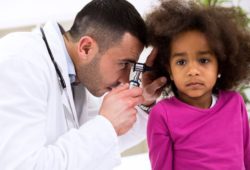 A doctor using a otoscope to look inside a young girls ear canal