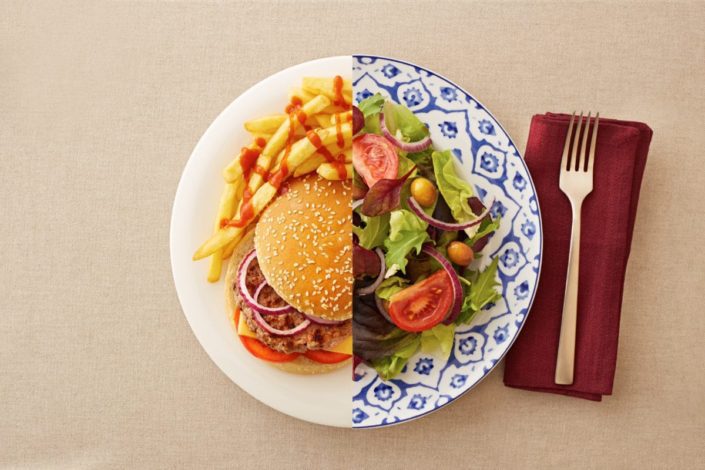 Unhealthy, high-carb burger and fries on one side of the plate and a healthy, low-carb salad on the other side.