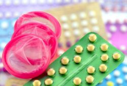 Condom and oral contraceptive pill on pharmacy counter with colorful pills strips background.