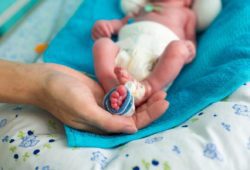 Mother holding premature baby’s feet with neonatal infant pulse oximeter