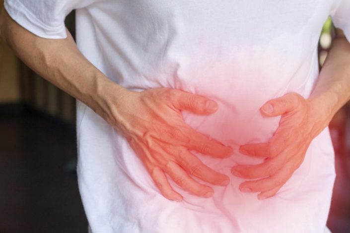 Man's hands on his stomach with red spot indicating pain caused by irritable bowel syndrome (IBS)