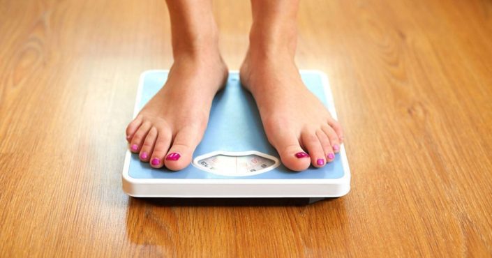 A person stands on a scale. Our BMI calculator can help measure your weight relative to your height and functions as a rough estimate of body fat.