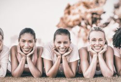 five women laying horizontally in a line on the ground holding their heads in the palms of their hands